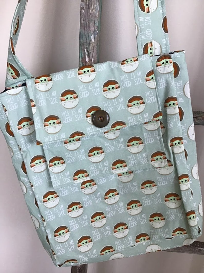 Puede incluir: Una bolsa de mano de color verde claro con un patr&oacute;n repetido de un personaje de dibujos animados con el texto "This is my good side".