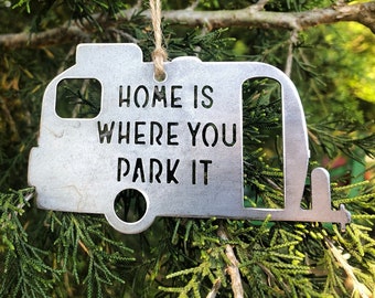 Könnte beinhalten: Ein silberner Wohnwagen-Anhänger aus Metall mit dem Text "Home is where you park it".