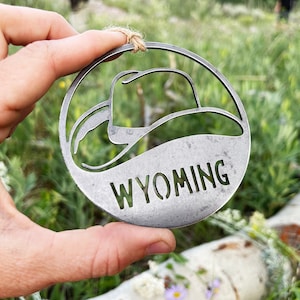 May include: A silver metal ornament shaped like a cowboy hat with the word "WYOMING" cut out in the center.