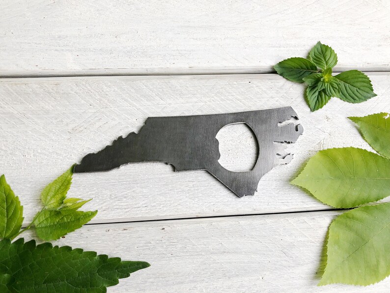 May include: A metal bottle opener shaped like the state of North Carolina. The opener has a hole in the center for opening bottles.
