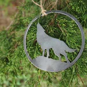 May include: A metal ornament shaped like a howling wolf, hanging from a branch of a green evergreen tree.