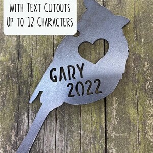 May include: A metal cardinal silhouette with a heart cutout and the name "GARY" and the year "2022" cut out. The text "ADD PERSONALIZATION WITH TEXT CUTOUTS UP TO 12 CHARACTERS" is in a white box.