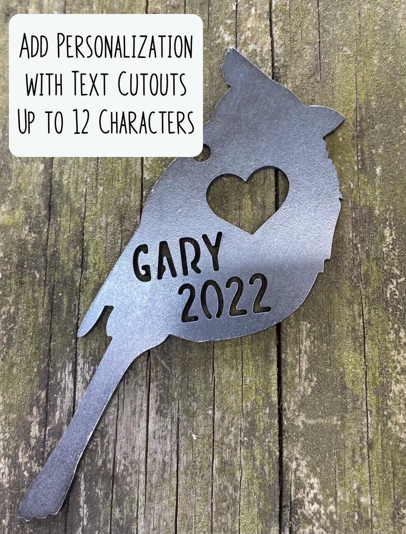 May include: A metal cardinal silhouette with a heart cutout and the name "GARY" and the year "2022" cut out. The text "ADD PERSONALIZATION WITH TEXT CUTOUTS UP TO 12 CHARACTERS" is in a white box.