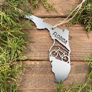 May include: A metal ornament shaped like the state of Florida with a bicycle silhouette inside and the word "FLORIDA" written on the ornament.