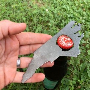 May include: A metal bottle opener shaped like the state of Virginia. The opener is being used to open a bottle of New Belgium beer.