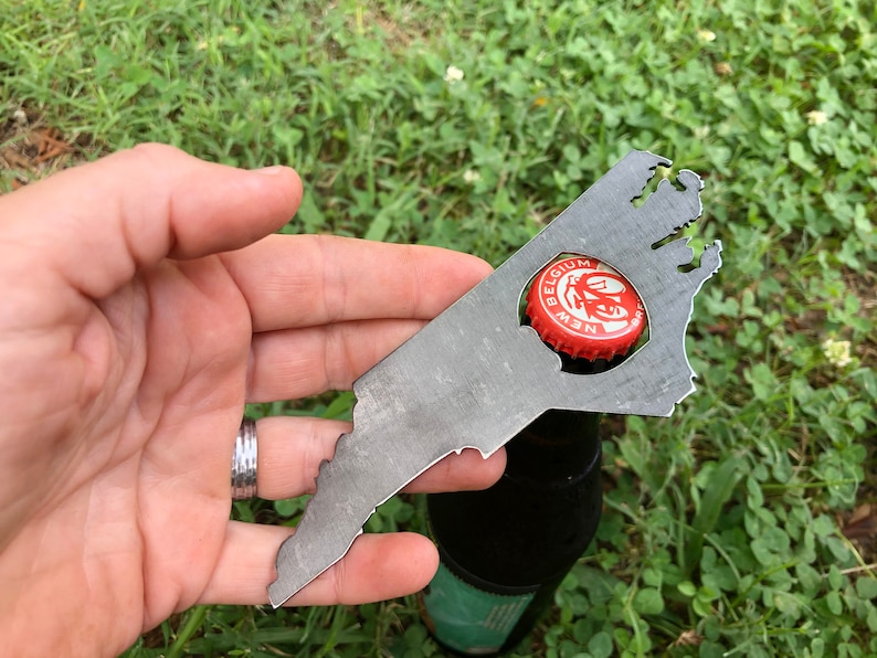 May include: A metal bottle opener shaped like the state of Virginia. The opener is being used to open a bottle of New Belgium beer.