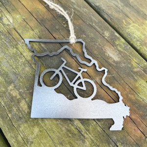 May include: A metal ornament shaped like the state of Missouri with a bicycle silhouette inside. The ornament is silver and has a twine string for hanging.