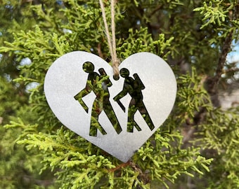 May include: A silver heart-shaped ornament with two hikers cut out of the metal. The ornament has a string for hanging.