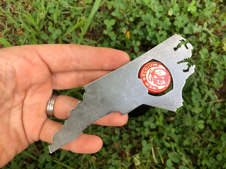 May include: A metal bottle opener shaped like the state of Virginia. The opener has a hole in the shape of a bottle cap, with a red and white bottle cap inside the hole. The bottle cap has the text "BELGIUM NEW BREWING" on it.