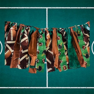May include: A festive banner with alternating fabric strips in brown, green, and tan. The strips are adorned with football and helmet patterns, creating a sporty and celebratory aesthetic. Perfect for a game day party.