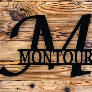 May include: Black metal monogram with the letter "M" and the name "MONTOUR" in a split design. The monogram is on a wood background.