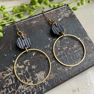 May include: A pair of gold hoop earrings with black leather accents. The hoops are simple and circular, and the leather accents are small and round.