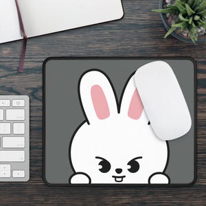 May include: A gray mousepad with a white cartoon rabbit design and a white computer mouse. The rabbit has pink inner ears and black eyes. The mousepad is rectangular and has a black border.