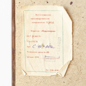 May include: A white label with black text that reads "Volgograd Production Enterprise OSVOD". The label also includes the text "Product: "Sunflowers"", "OST 25-565-75", "TO-133-76", "Art. C-B-301a", "Retail price 6-00", "Stamp ОТК", and "Order 5744-1000g".