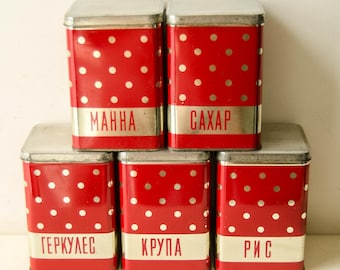 May include: Five vintage red metal canisters with white polka dots and silver lids. Each canister has a silver label with Cyrillic text. The canisters are arranged in a stack, suggesting kitchen storage or organization.