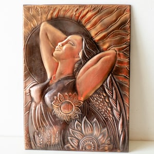 May include: A copper wall sculpture of a woman with her arms raised, surrounded by sunflowers and wheat. The sculpture has a textured, hammered finish.