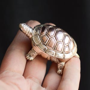 May include: A silver-colored turtle figurine with a detailed shell pattern. The turtle's head and legs are also intricately designed. The figurine is made of metal and has a shiny finish. The turtle is a decorative item.