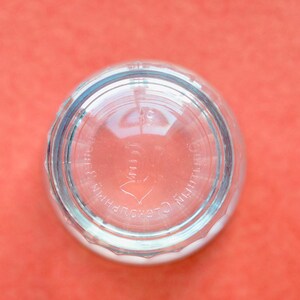 Op de afbeelding: Een helder glazen voorwerp van onderen bekeken, met een ronde bodem en een gegoten patroon. De reli&euml;ftekst op de onderkant luidt "DURALEX" en "MADE IN FRANCE", samen met een klein cijfer, zichtbaar door het transparante glasmateriaal.