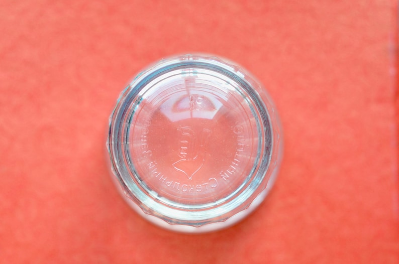 Op de afbeelding: Een helder glazen voorwerp van onderen bekeken, met een ronde bodem en een gegoten patroon. De reli&euml;ftekst op de onderkant luidt "DURALEX" en "MADE IN FRANCE", samen met een klein cijfer, zichtbaar door het transparante glasmateriaal.