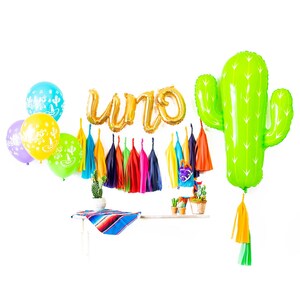 May include: A green cactus balloon with a tassel, gold foil balloons spelling "UNO", colorful tissue paper tassels, and a variety of balloons in yellow, blue, and purple.