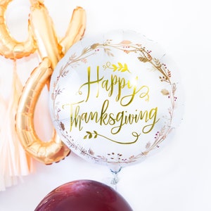 May include: A silver balloon with a gold "Happy Thanksgiving" message and a floral design. There are two maroon balloons and a gold foil balloon in the background.