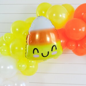 Op de afbeelding: Een ballonboog gemaakt van witte, gele en oranje ballons. Een grote oranje, gele en witte ma&iuml;sballon met een glimlachend gezicht bevindt zich in het midden van de boog.