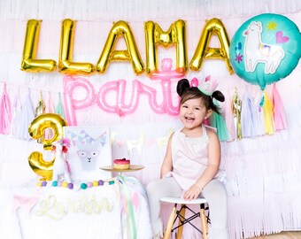 May include: A young girl wearing a pink dress and a llama party hat sits on a white stool in front of a pink and white backdrop.  The backdrop is decorated with gold foil letters spelling "llama party" and a blue balloon with a llama illustration.  There is a gold number 3 balloon on the table in front of her.