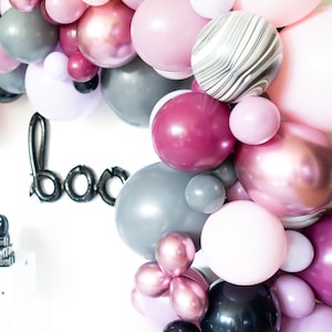 May include: A garland of balloons in shades of pink, gray, and maroon. The balloons are arranged in a circular shape and have a variety of textures, including marble, metallic, and matte.