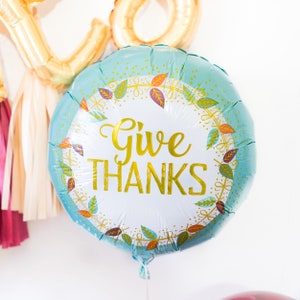 May include: A blue and gold foil balloon with a white circle in the center. The circle has a gold wreath with leaves and the text "Give THANKS" in gold lettering.