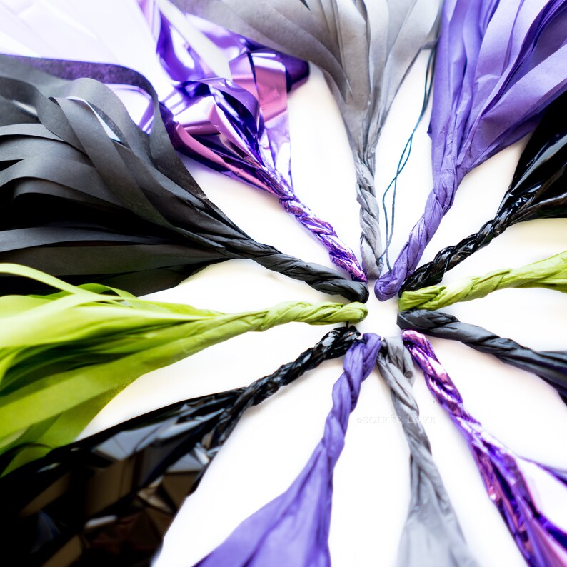 May include: A collection of tissue paper streamers in black, green, and purple colors. The streamers are twisted together in a circular pattern, creating a festive and decorative display.
