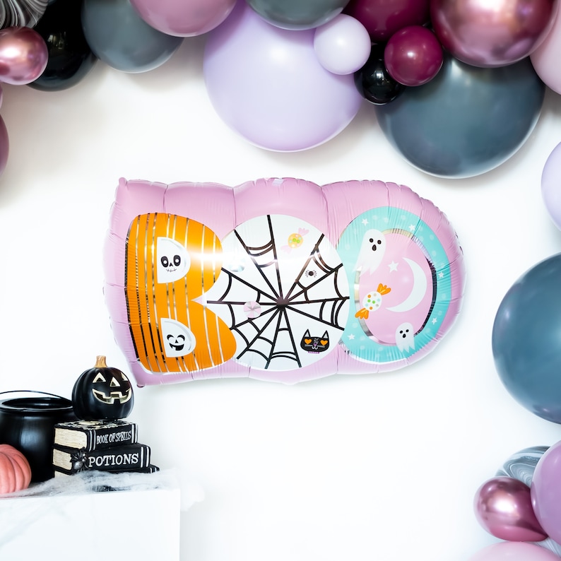 May include: A pink, orange, and blue BOO balloon with a spiderweb, ghost, and candy corn design. The balloon is surrounded by a garland of purple, pink, and gray balloons.
