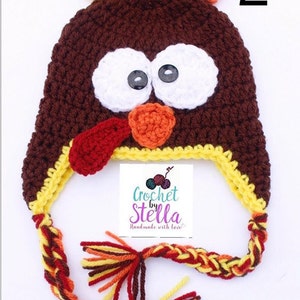May include: Crocheted turkey hat with a brown body, white eyes, orange beak, and red wattle. The hat has a yellow and brown braided strap with tassels. The hat is labeled "Crochet by Stella Handmade with love".