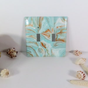 May include: A decorative double light switch cover with a marbled design in shades of teal, white, and copper. The cover has two switch openings and is surrounded by seashells and a starfish.