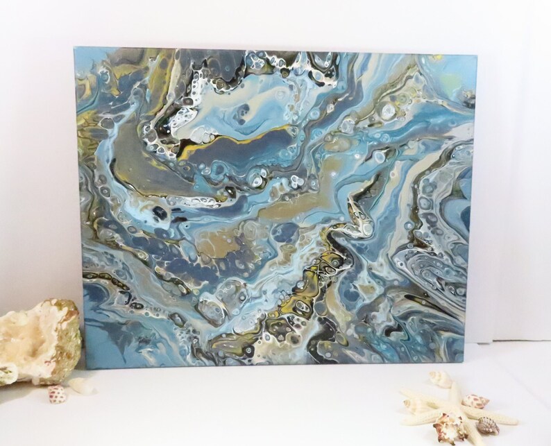 May include: Abstract acrylic painting on canvas with a fluid art design. The artwork features a blend of blues, grays, and gold, creating a marbled effect. The painting is a square format, suitable for wall decor.