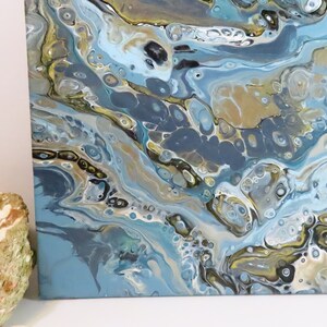 May include: Abstract acrylic painting on canvas with a fluid design. The artwork features a blend of blues, gold, and gray hues, creating a marbled effect. The painting's texture and color palette evoke a sense of depth and movement, suitable for home decor.