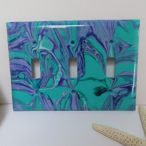 May include: A light switch plate with a teal, purple, and white abstract marbled design. The plate has three toggle switches.