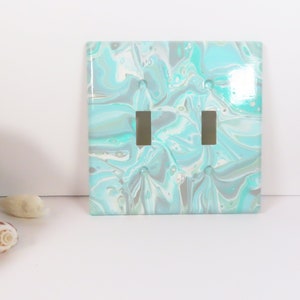 May include: A light blue and white marbled double light switch cover. The cover has a glossy finish and is made of ceramic.
