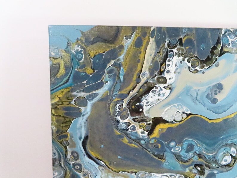 May include: Abstract acrylic painting on canvas with a fluid design. The artwork features a blend of blue, gray, white, and gold hues, creating a marbled effect. The colors swirl and mix, forming organic shapes and patterns. The canvas is square.