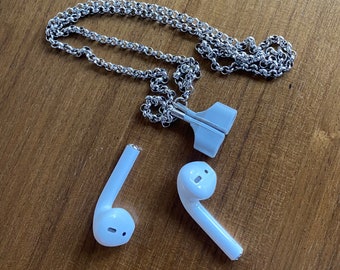 Puede incluir: Un collar de cadena plateado con un accesorio de plástico blanco. También se muestran dos puntas de auriculares inalámbricos blancos.