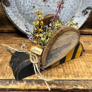 May include: Wooden bee figurine with black and yellow stripes, decorated with dried flowers and a small sign that says "Queen".