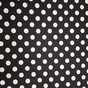 May include: Black fabric with a repeating pattern of large white polka dots. The fabric is laid out flat, showing the full pattern. The polka dots are evenly spaced and create a classic, playful design. The fabric is likely used for clothing or home decor.