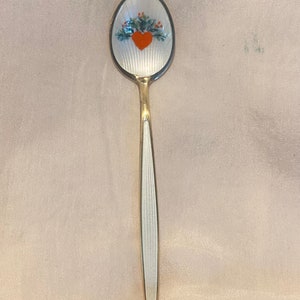 May include: A silver teaspoon with a white enamel finish and a hand-painted design of a red heart with green leaves.