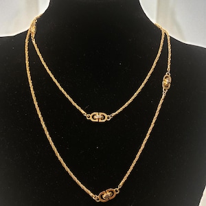 May include: A gold-toned necklace set displayed on a black mannequin. The set includes two necklaces of different lengths, both featuring a rope chain design. Each necklace has a decorative element with a double-C design.