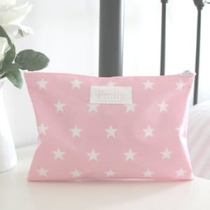 Puede incluir: Bolsa rosa con cremallera con un patrón de estrellas blancas y el nombre "Emily" impreso en una etiqueta blanca.