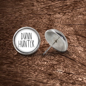 May include: A pair of silver stud earrings with a white background and the text "Dunn Hunter" in black.