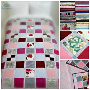 Op de afbeelding: Een patchworkdeken met een geruit patroon in roze, rood, wit en zwart. De deken is gemaakt van verschillende stoffen, waaronder bloemenprints, strepen en effen stoffen. De deken wordt getoond op een bed met witte beddengoed.