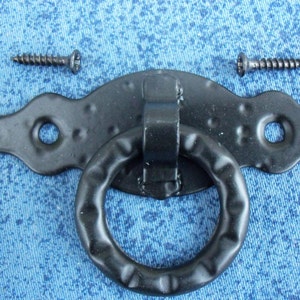 Peut inclure: Poignée de tirage en métal noir avec deux vis. La poignée a une surface texturée et un anneau décoratif.