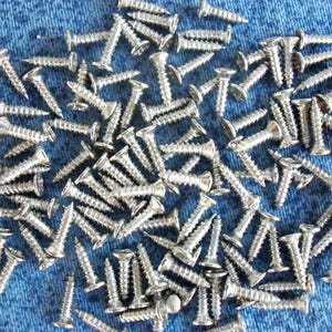 Pode incluir: Um conjunto de parafusos prateados com cabeças chatas e hastes roscadas, sobre tecido denim azul. Os parafusos são de vários tamanhos, adequados para projetos de carpintaria ou construção em geral.