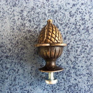 May include: A gold-toned metal acorn finial with a decorative, textured top and a screw base.