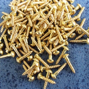 May include: A pile of gold-coloured screws with round heads. The screws are arranged in a random pattern on a blue denim background.